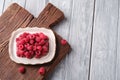 Raspberry fruits in plate on old teak cutting board, healthy pile of summer berries on wooden background