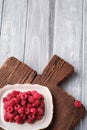 Raspberry fruits in plate on old teak cutting board, healthy pile of summer berries on wooden background