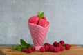 Raspberry ice cream sorbet in pink porcelaine cone with raspberry, mint leaves copy space on wooden plank and grey textured back Royalty Free Stock Photo