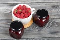 Raspberry jam in glass jars. Nearby are raspberries in a large white mug. On wooden boards with a beautiful texture