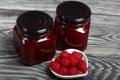 Raspberry jam in glass jars. Nearby are raspberries in a saucer. On wooden boards with a beautiful texture