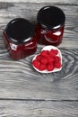 Raspberry jam in glass jars. Nearby are raspberries in a saucer. On wooden boards with a beautiful texture