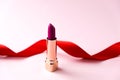 Raspberry lipstick on a pink background, in the background a red swirling ribbon. Beauty. Holiday gift