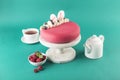 Raspberry mousse cake on a white wooden stand with a teapot and a cup of tea on a bright green background Royalty Free Stock Photo