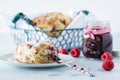 Raspberry scone on a small plate with a jar of raspberry jam and a basket of scones in behind.