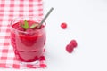 Raspberry smoothie in a glass with a metal straw on a red and white checkered tablecloth. Three raspberry berries on a white