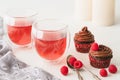 Raspberry tea in glass cups and chocolate cupcakes decorated with chocolate frosting and fresh raspberries close up on white backg Royalty Free Stock Photo