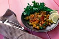Ratatouille on a black plate, colored different vegetables in a stew, with fresh parsley leaves and lemon slices, on a pink wooden