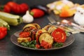 Ratatouille is located on a plate on a dark background. Baked vegetables: aubergines, zucchini and tomatoes