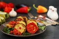 Ratatouille is located on a plate on a dark background. Baked vegetables: aubergines, zucchini and tomatoes