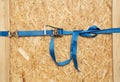 Ratchet truck cargo tie downs clasp chipboard box. Blue load belt over wooden osb surface Royalty Free Stock Photo