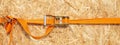 Ratchet truck cargo tie downs clasp chipboard box. Orange load belt over wooden osb surface