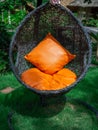 Rattan lounger hanging egg chair with orange pillow Royalty Free Stock Photo