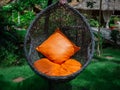 Rattan lounger hanging egg chair with orange pillow Royalty Free Stock Photo