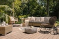 A rattan patio set including a sofa, a table and a chair on a wooden deck in the sunny garden.