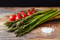 Raw asparagus stems with a brunch of cherry tomatoes and a pinch of coarse sea salt on a rustic wooden table with black background Royalty Free Stock Photo