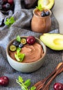 Raw avocado chocolate mousse topped with chocolate pieces, cherry, blueberry and mint, selective focus. Grey background. Healthy