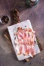 Raw bacon slices on paper on a cutting board on the table. Hearty snack. Top and vertical view