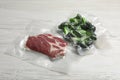 Raw beef and broccoli in vacuum packs on white wooden table