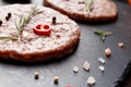 Raw beef cutlets for burgers, rosemary, vegetables and spices on a stone plate on a dark background