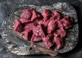 Raw beef fillet meat pieces for stew on a wooden rustic cutting board on dark background, top view Royalty Free Stock Photo