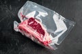 Raw beef meat Club or striploin on the bone steak in plastic airtight pack, on black stone background, with copy space for text