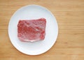 Raw beef meat on white plate against wooden backgroundwith copy space. Top view