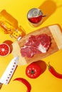 Raw beef meat on a wooden board and ingredients for cooking on a yellow background