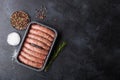 Raw beef and pork sausage in plastic tray with salt and pepper on black background. Space for text Royalty Free Stock Photo