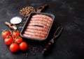 Raw beef and pork sausage in plastic tray with vintage fork on black background.Salt and pepper with tomatoes and rosemary Royalty Free Stock Photo