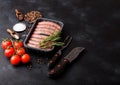 Raw beef and pork sausage in plastic tray with vintage knife and fork on black background.Salt and pepper with tomatoes and Royalty Free Stock Photo