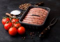 Raw beef and pork sausage in plastic tray with vintage fork on black background.Salt and pepper with tomatoes and rosemary Royalty Free Stock Photo