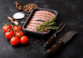 Raw beef and pork sausage in plastic tray with vintage knife and fork on black background.Salt and pepper with tomatoes and Royalty Free Stock Photo