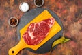 Raw beef ribeye on a round slate plate with glass containers containing peppercorns  coarse salt and cayenne chillies on an old Royalty Free Stock Photo