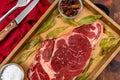 Raw beef ribeye on a round slate plate with glass containers containing peppercorns, coarse salt and cayenne chillies on an old Royalty Free Stock Photo