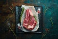 Raw beef ribeye steak on the bone with thyme, rosemary and spices. Flat lay top view on black stone cutting table Royalty Free Stock Photo