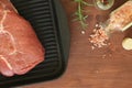 Raw beef rump steak on heavy iron grill pan on wooden board. Sprig of fresh rosemary, glass bottles with peppercorns and salt Royalty Free Stock Photo