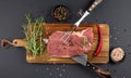 Raw beef steak cooking with knife and fork for meat and fresh rosemary and spice on wooden cutting board, black background Royalty Free Stock Photo