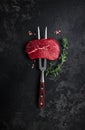 Raw beef steak on a fork with rosemary and spices on a dark background. Preparing fresh beef steak, vertical image. top view.