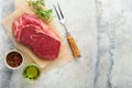 Raw beef steak. Fresh beef rib eye steak with fork rosemary, salt and pepper on piece of parchment paper on dark grey stone backgr Royalty Free Stock Photo