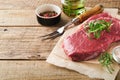 Raw beef steak. Fresh beef rib eye steak with fork rosemary, salt and pepper on piece of parchment paper on old wooden background Royalty Free Stock Photo