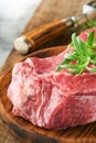 Raw beef steak. Fresh beef rib eye steak with fork rosemary, salt and pepper on piece of parchment paper on old wooden background. Royalty Free Stock Photo