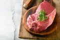 Raw beef steak. Fresh beef rib eye steak with fork rosemary, salt and pepper on piece of parchment paper on old wooden background. Royalty Free Stock Photo