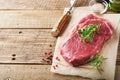 Raw beef steak. Fresh beef rib eye steak with fork rosemary, salt and pepper on piece of parchment paper on old wooden background Royalty Free Stock Photo