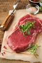 Raw beef steak. Fresh beef rib eye steak with fork rosemary, salt and pepper on piece of parchment paper on old wooden background Royalty Free Stock Photo