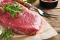 Raw beef steak. Fresh beef rib eye steak with fork rosemary, salt and pepper on piece of parchment paper on old wooden background. Royalty Free Stock Photo