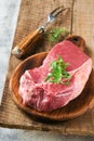 Raw beef steak. Fresh beef rib eye steak with fork rosemary, salt and pepper on piece of parchment paper on old wooden background Royalty Free Stock Photo