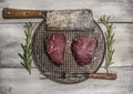 Raw beef steak on an iron pan with rosemary, meat cleaver and fork on bright, rustic wood background top view close up Royalty Free Stock Photo