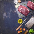 Raw beef steak with rosemary,butter and meat fork on dark rustic cutting board, top view