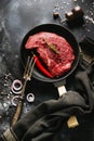 Raw beef steak with spices, onions and chili in cast-iron frying pan for frying on dark slate or concrete background. Royalty Free Stock Photo
